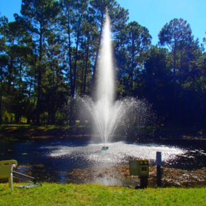 The EFL-350 Lighted Lake Fountain sprays 25'H x 30'W in a pond surrounded by grass and tall trees under clear skies.